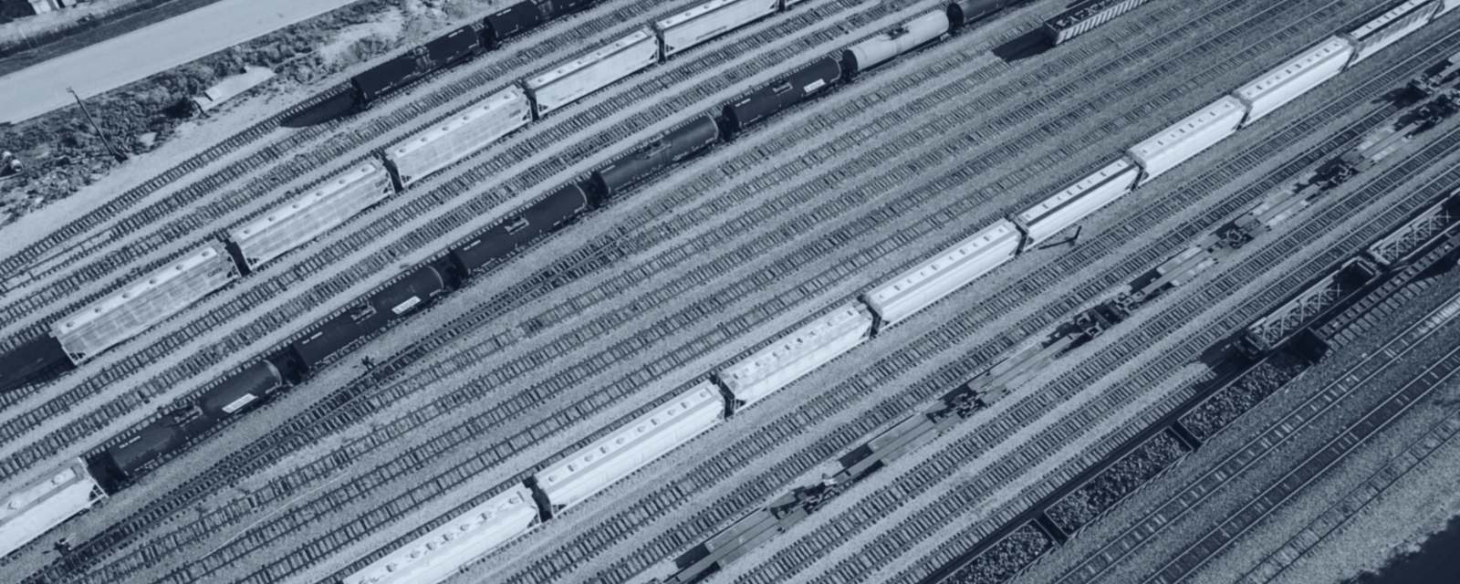 Rows of freight wagons across a rail yard from above, slate duotone — atmospheric imagery